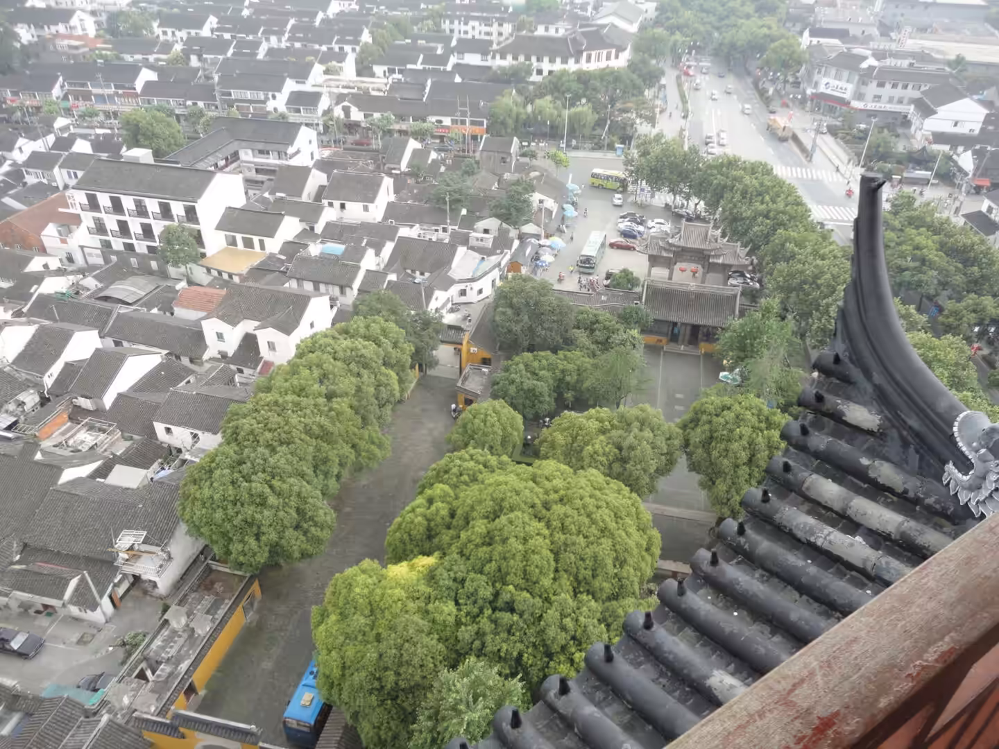 View over Suzhou’s old town from a pagoda, with white-walled houses, green trees, and tiled rooftops below