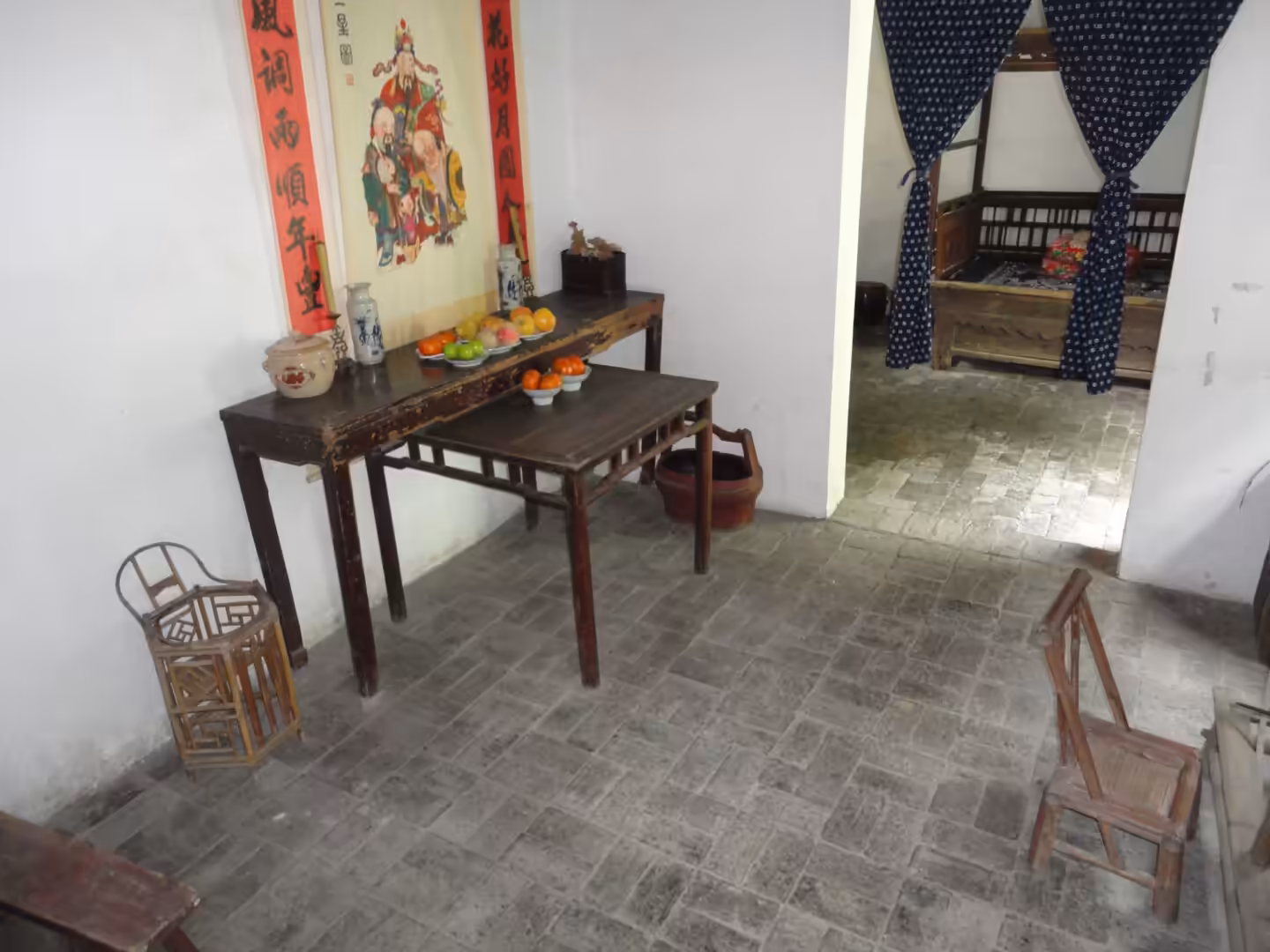 Simple altar table with fruit offerings and scroll painting inside a traditional home interior.