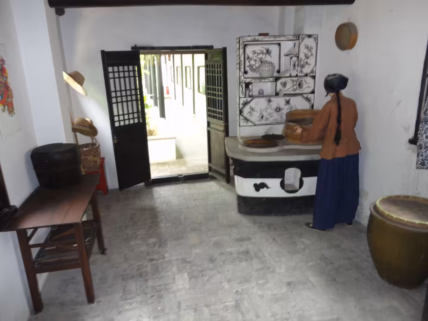 Reconstructed traditional kitchen interior with a woman figure preparing food at a masonry stove.