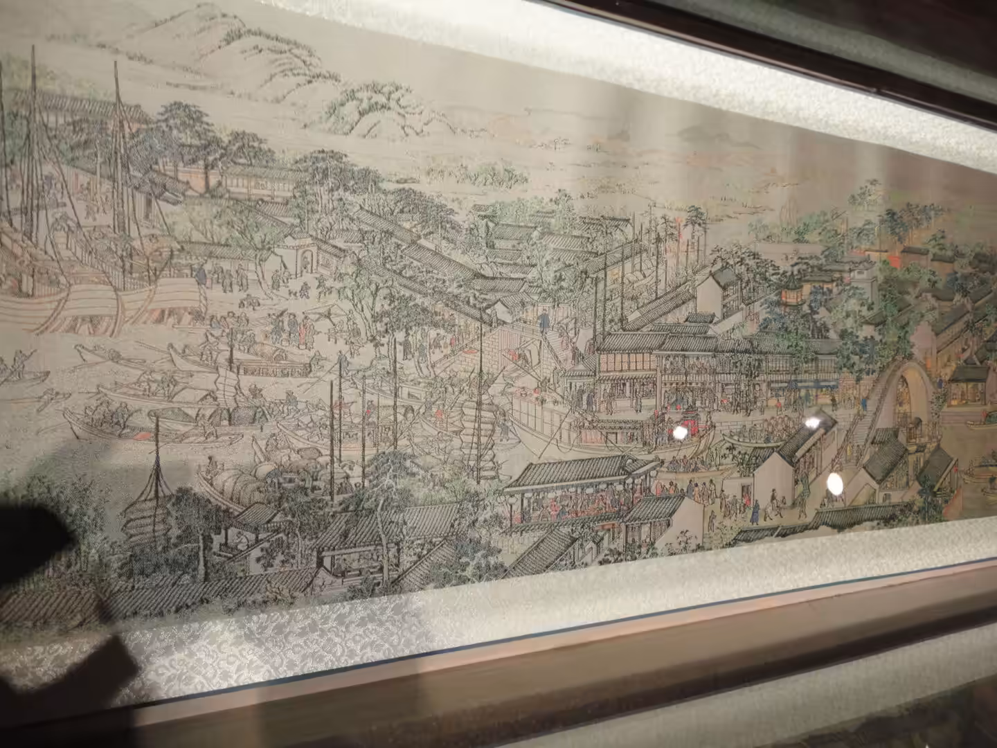 Panoramic traditional Chinese scroll painting depicting a bustling riverside town with bridges, boats, markets, and daily life scenes.