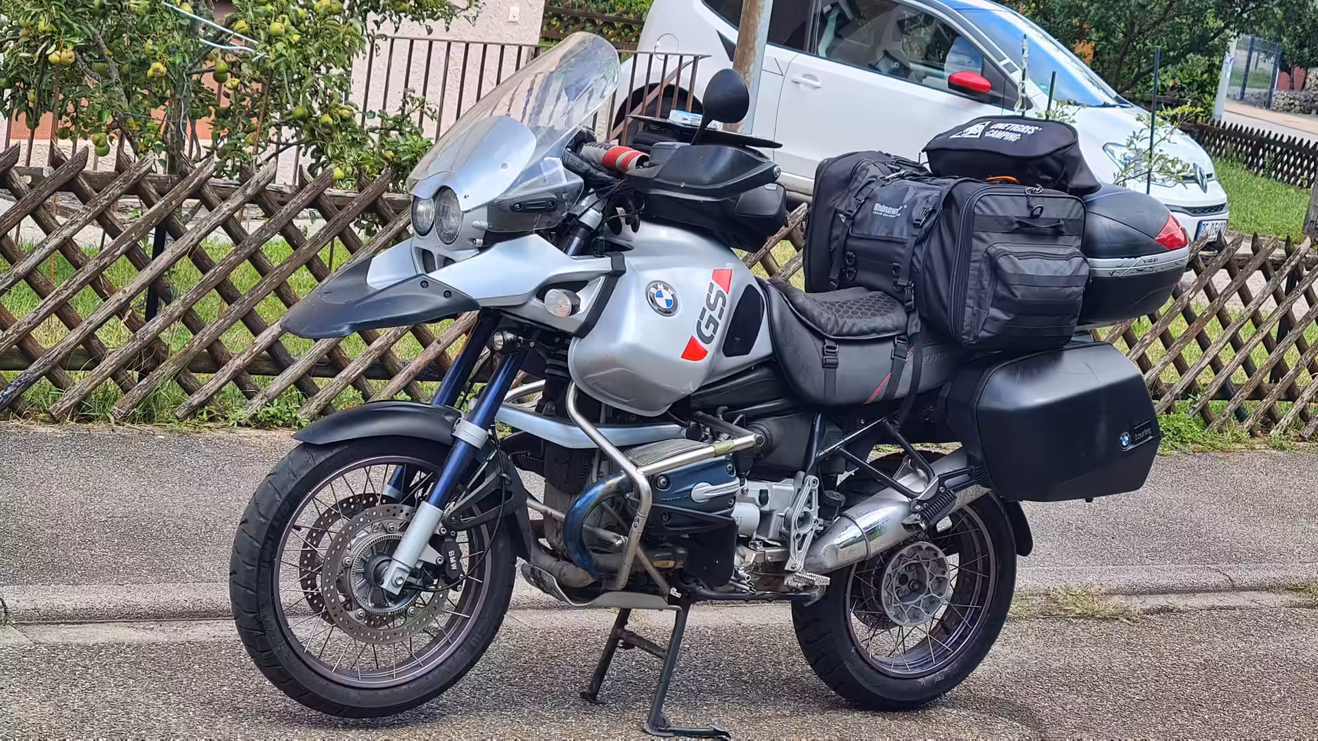 Fully equipped BMW R 1150 GS Adventure touring motorcycle with panniers, top case, luggage bags, and windshield parked beside a residential street.