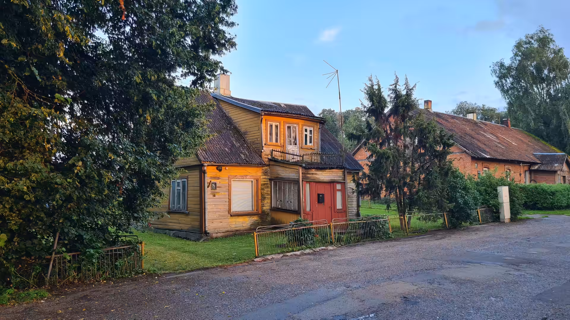 A traditional wooden house illuminated by the evening sun in a quiet Lithuanian village after rainfall.
