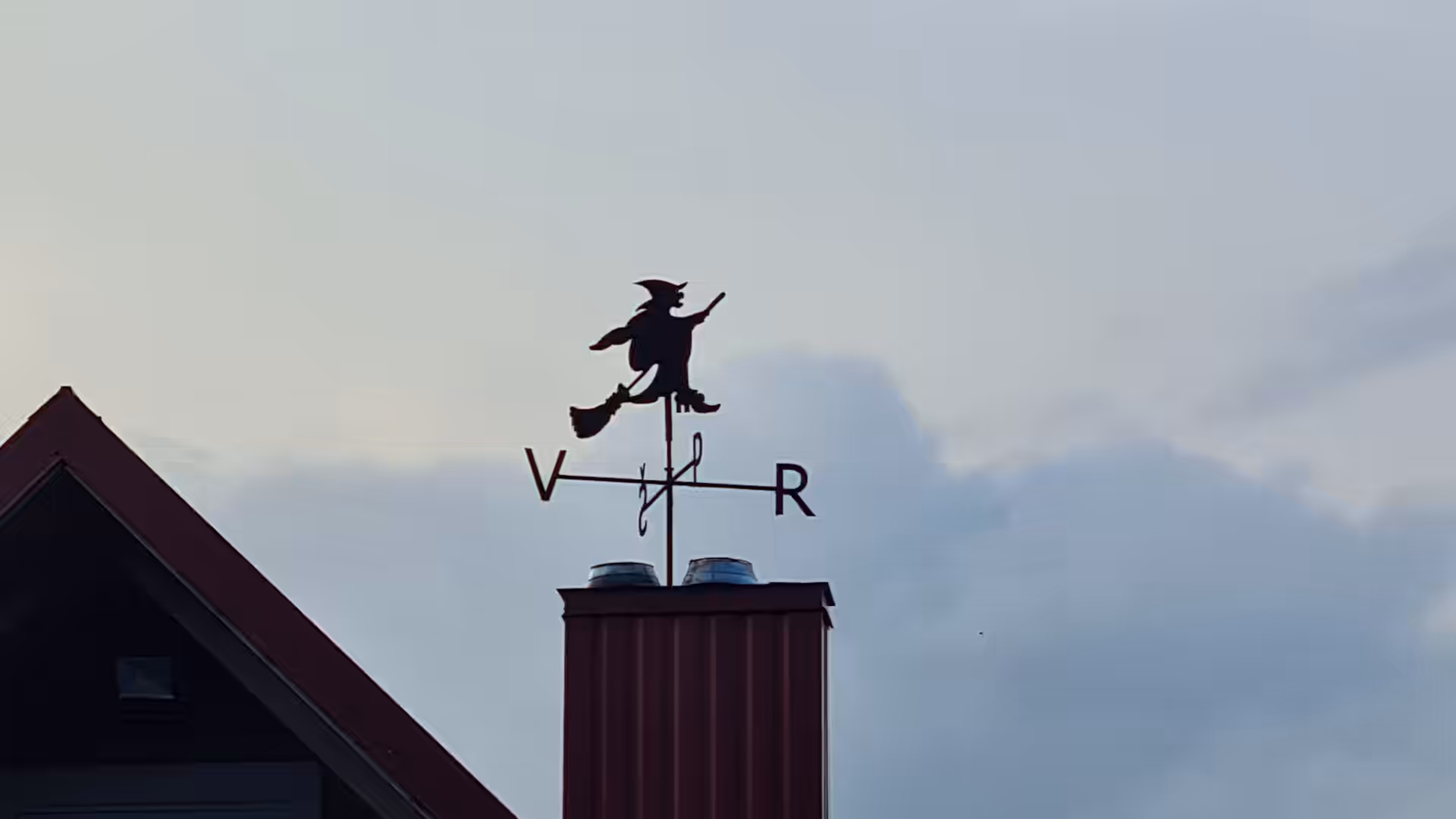 A decorative weather vane shaped like a witch riding a broom on the roof of a traditional house in Lithuania.