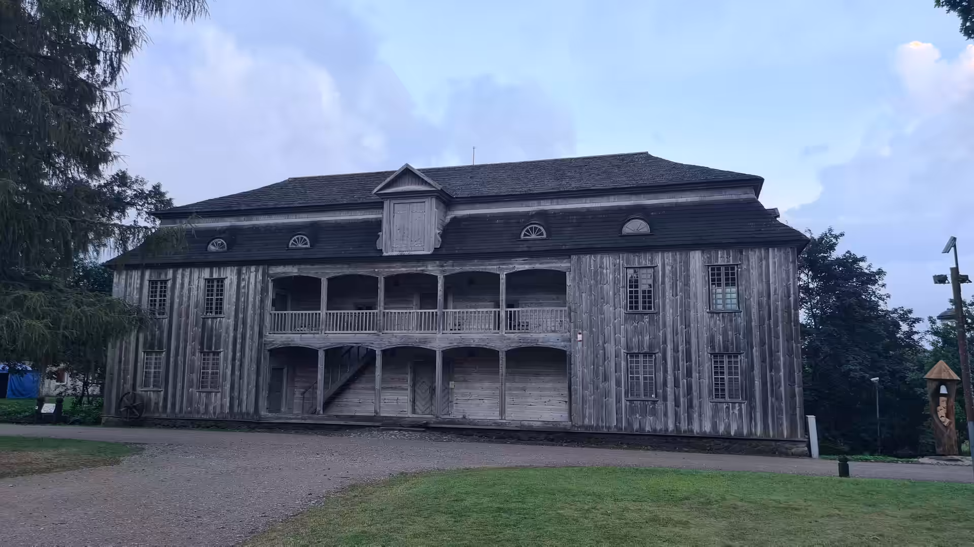 A large historic wooden manor house with two-story balconies in the Lithuanian countryside during the evening.