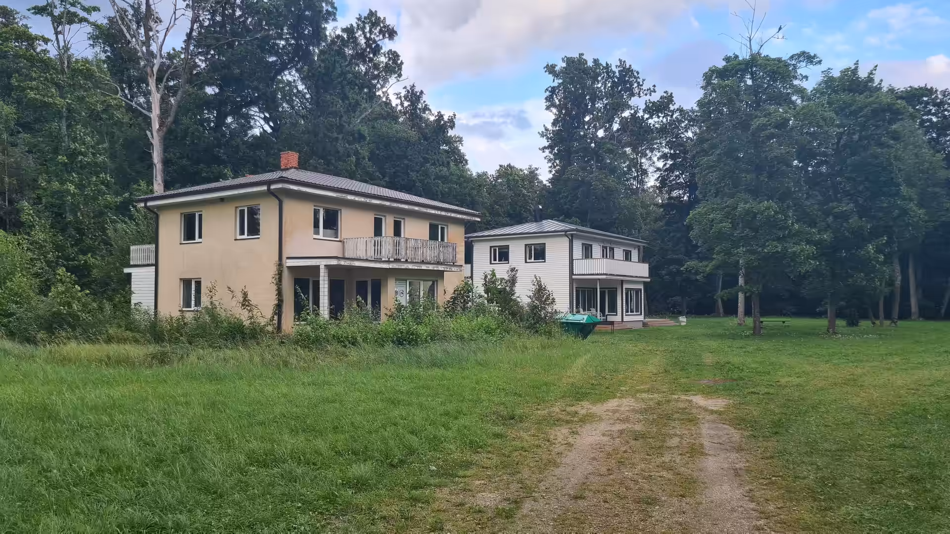 Two guesthouses surrounded by trees and open green space in a peaceful natural setting in Estonia.