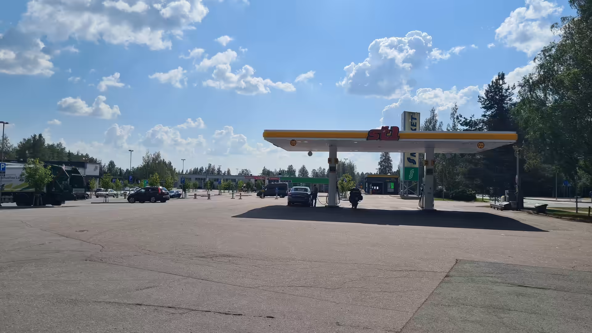 A red touring motorcycle stands at a fuel pump beneath a bright summer sky, at Lahti in Finland.