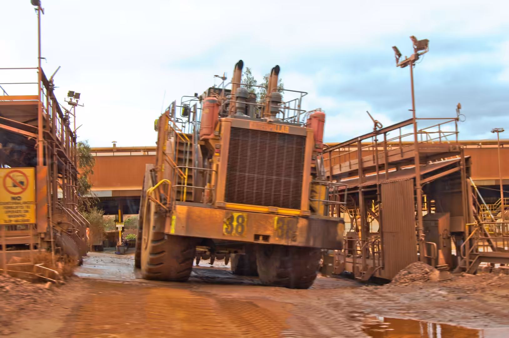 A massive rust-orange haul truck sits in a wet red mud yard.
