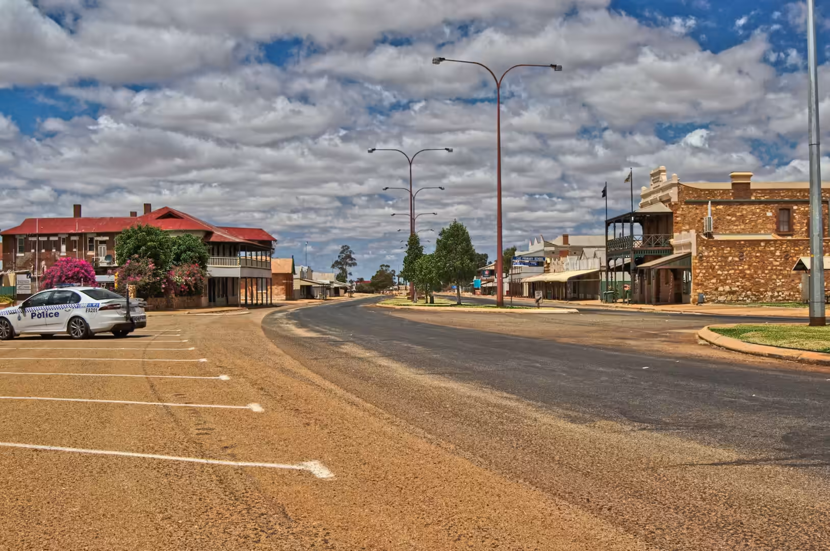 A quiet heritage town street lined with old verandahed buildings and a parked police car.
