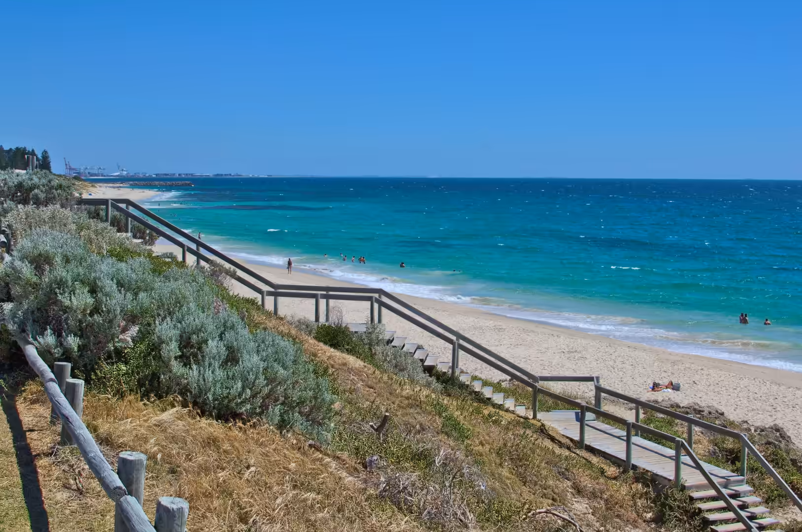 A wooden boardwalk zigzags down a dune to a turquoise beach.