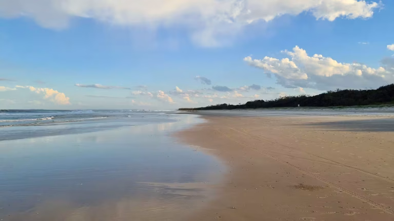 A long, empty beach reflects the blue sky in its wet sand.