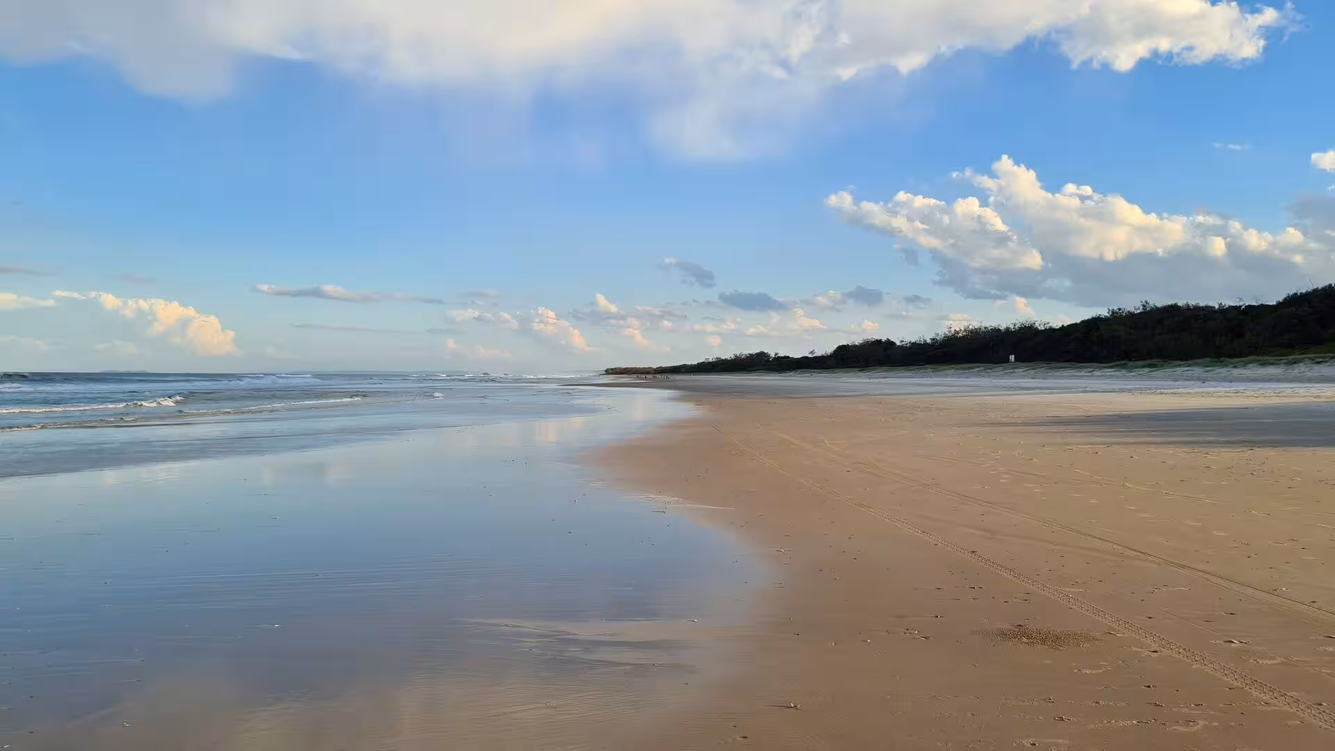 A long, empty beach reflects the blue sky in its wet sand.