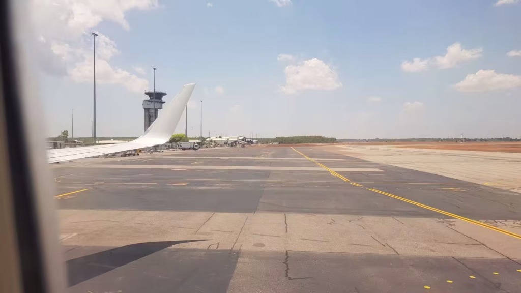 A white wing crosses an empty taxiway with an air-traffic tower ahead.