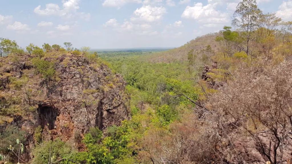 A broad escarpment overlooks a forested valley sweeping toward distant plains.