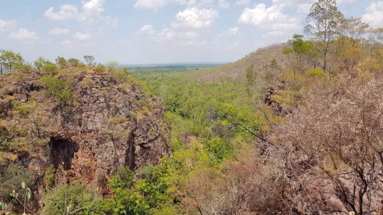 A broad escarpment overlooks a forested valley sweeping toward distant plains.