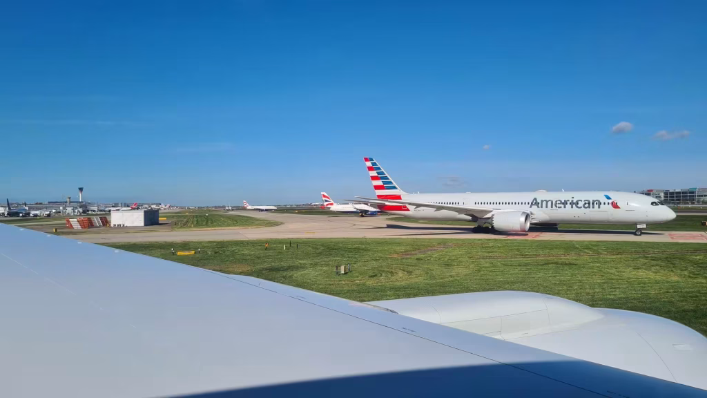 A widebody American Airlines plane taxis past a window seat on the runway.