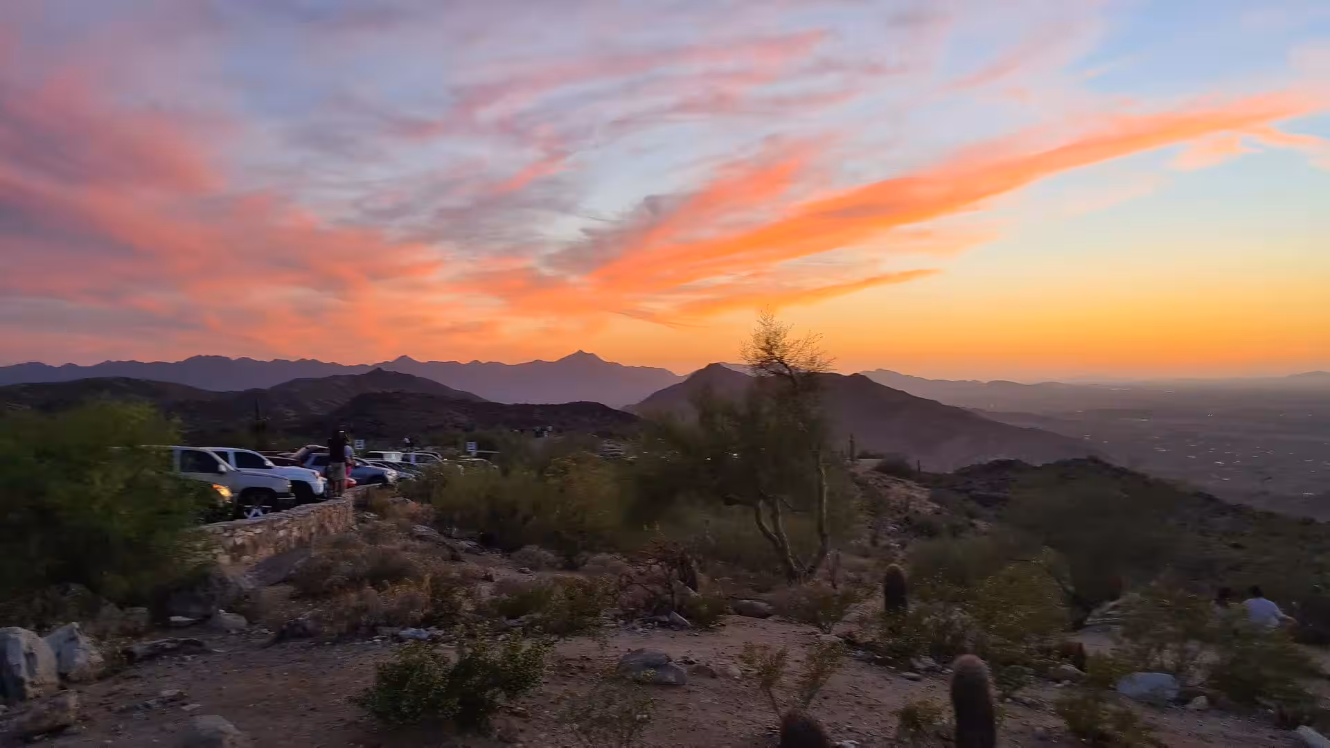 A rocky desert overlook glows under a fiery orange and pink sunset sky.