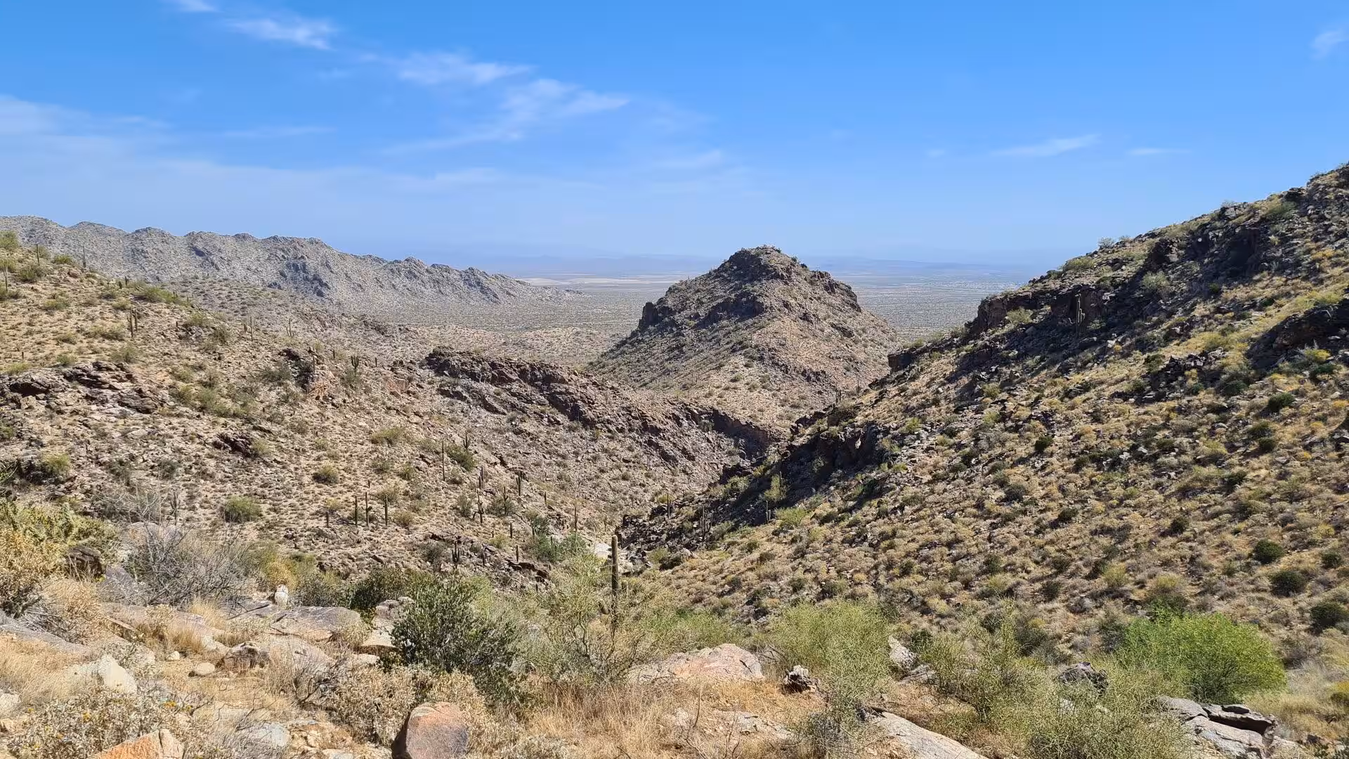 Jagged desert ridges and a central rock peak rise above a barren valley.