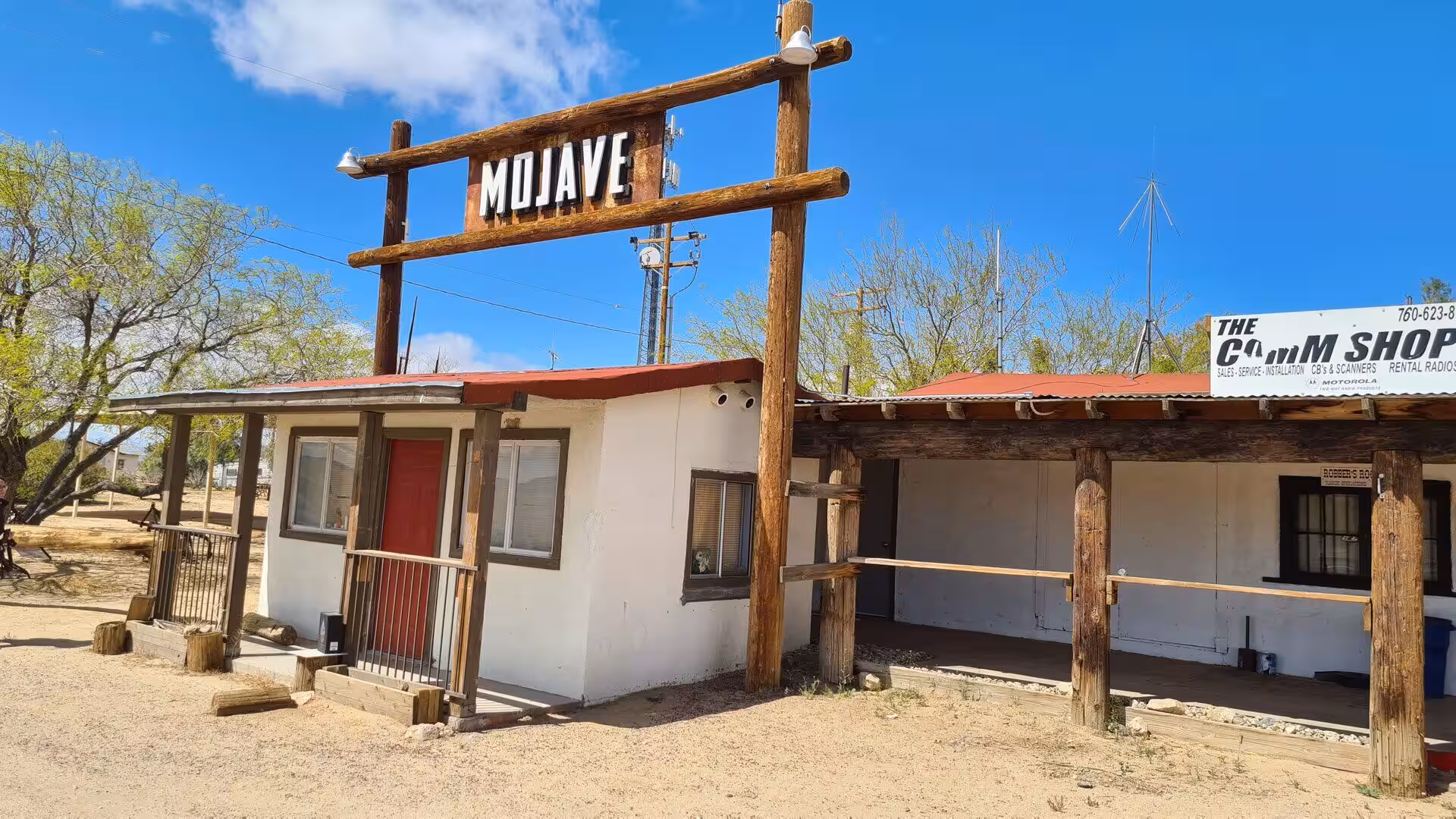A rustic wooden archway reading MOJAVE stands over a white shop with a red roof.