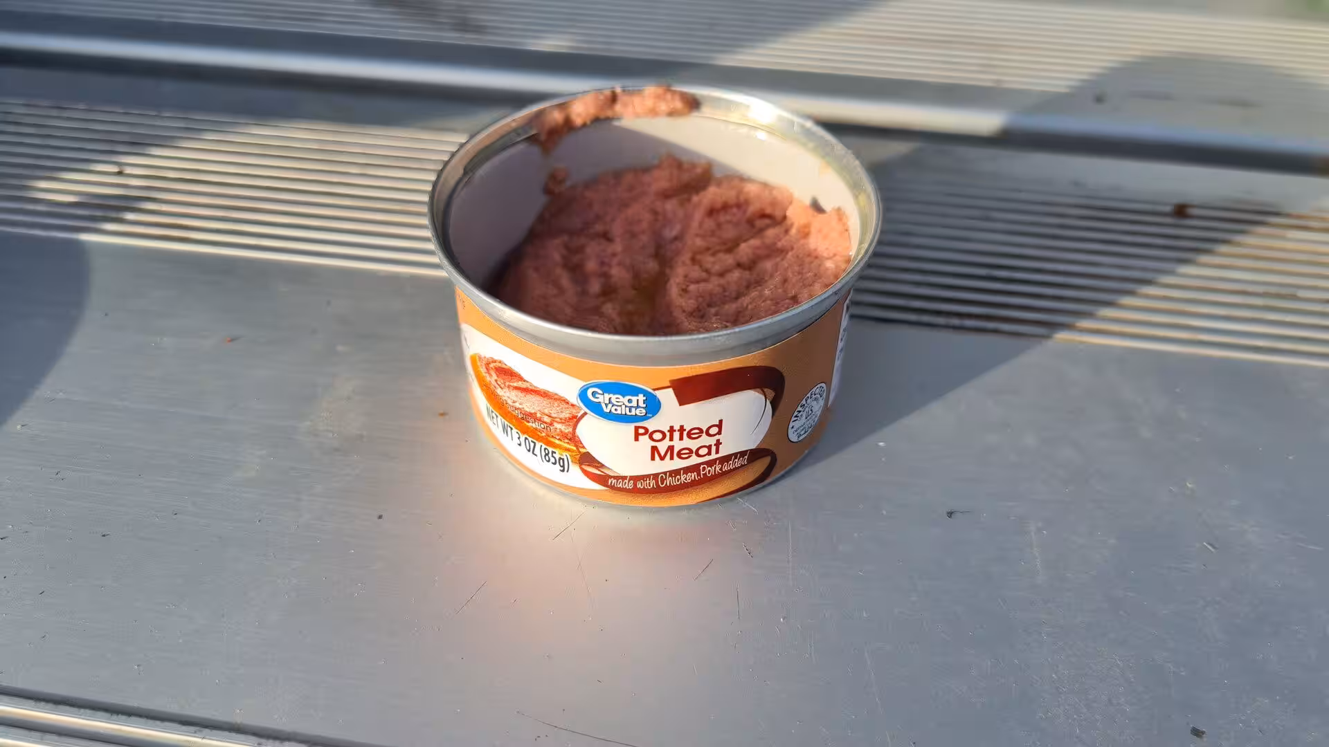 An open tin of Great Value potted meat sits on a grey metal surface.