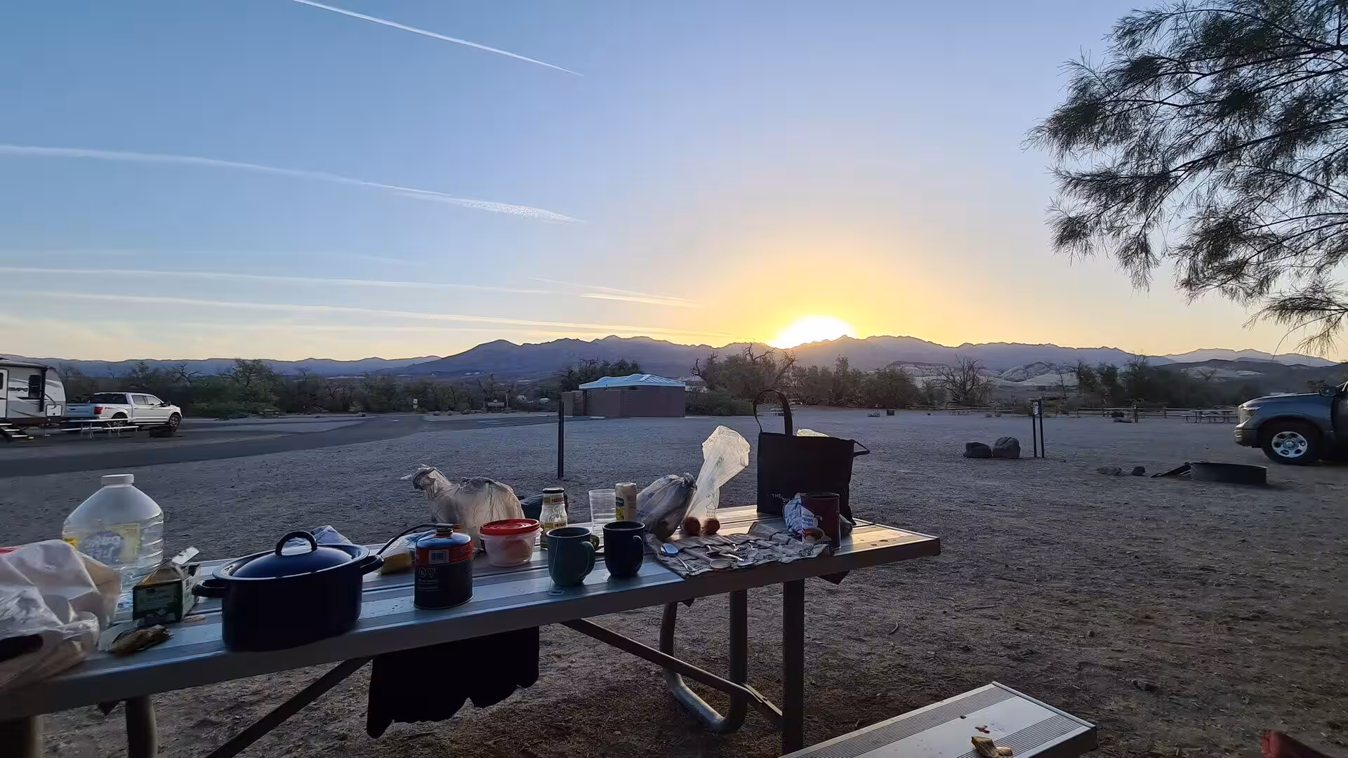 A picnic table loaded with pots and cooking gear sits at a desert campsite.