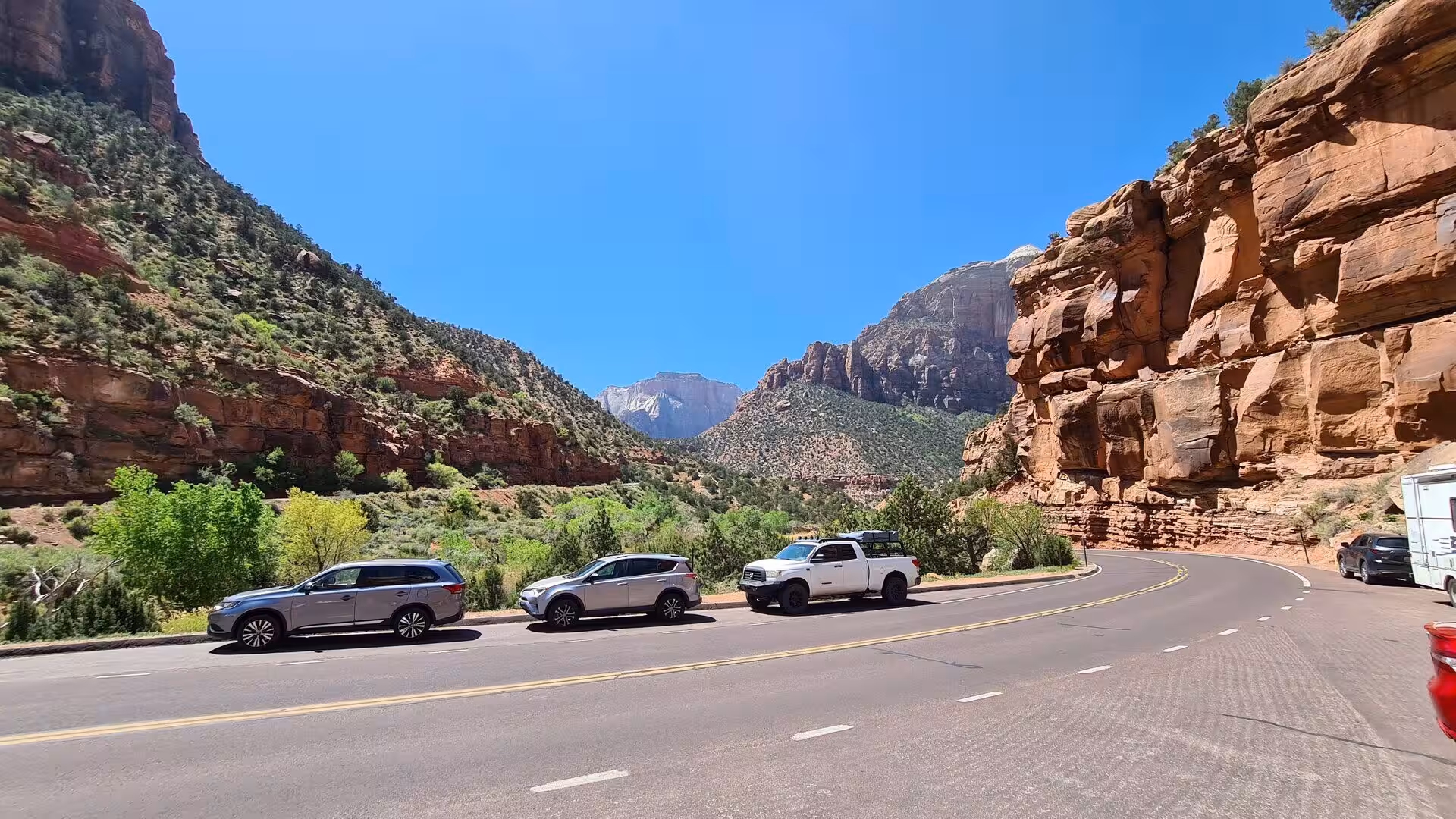 A line of cars waits on a road through a red rock canyon.