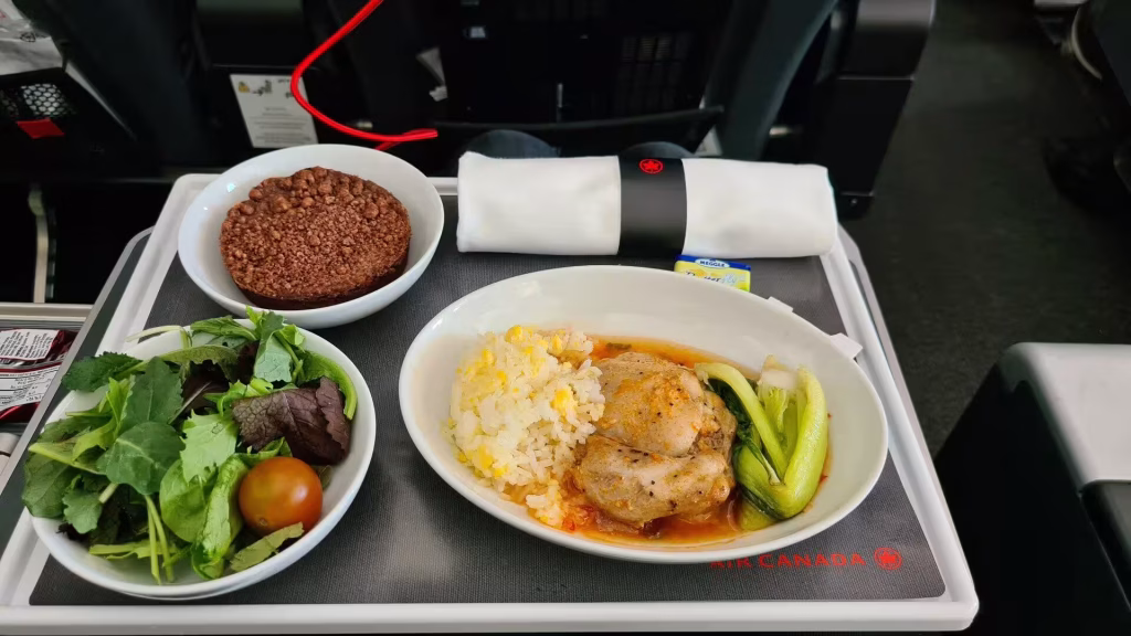 An Air Canada meal tray holds chicken, rice, greens, and a chocolate dessert.