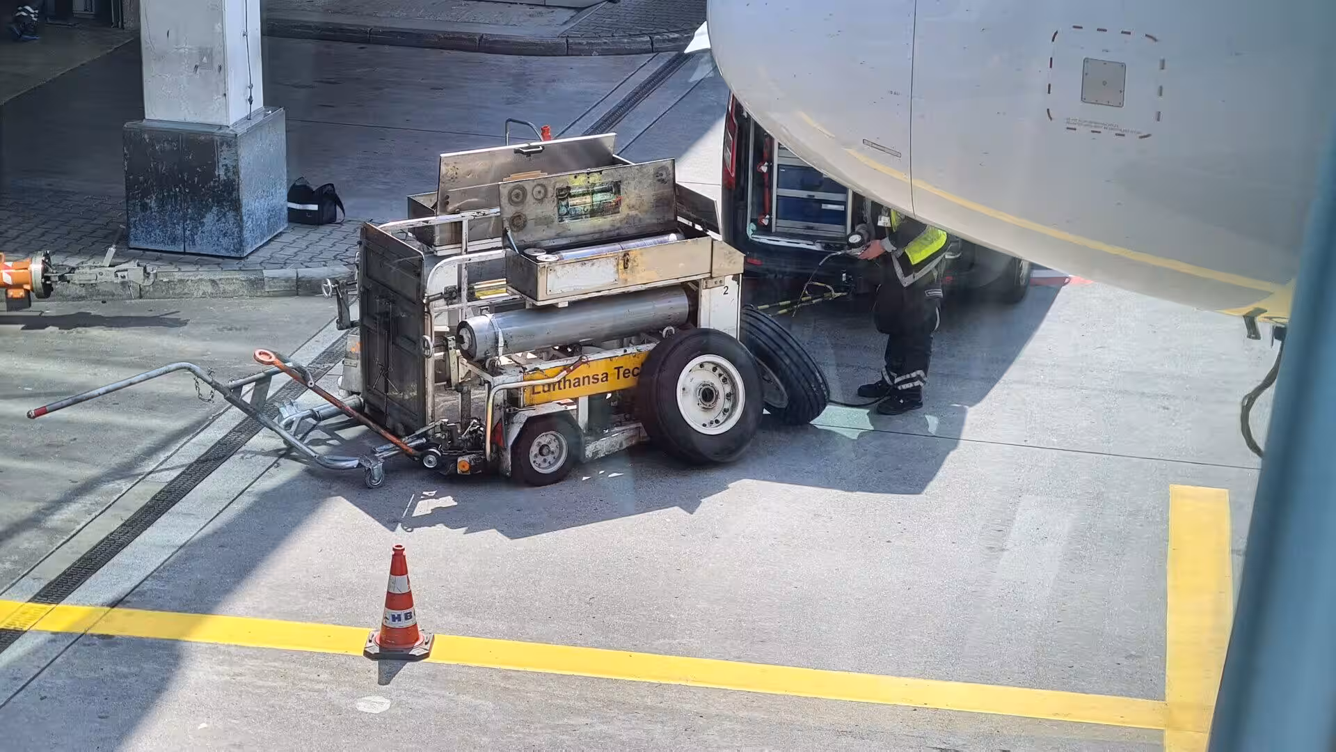 A Lufthansa Technik service cart sits beside an open aircraft panel as a worker attends the jet