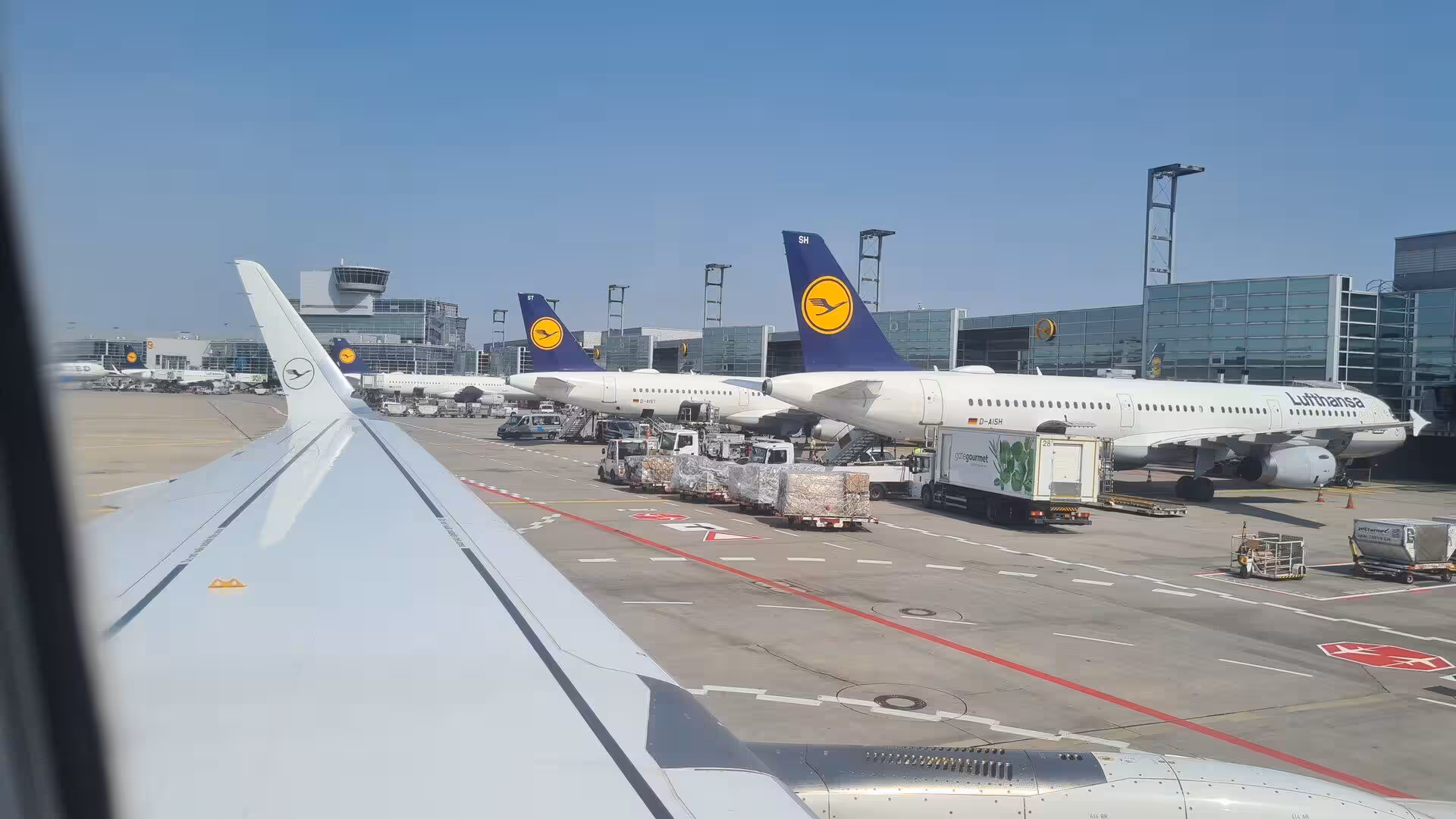 A line of Lufthansa narrow-body aircraft lines the terminal beyond the plane's wingtip