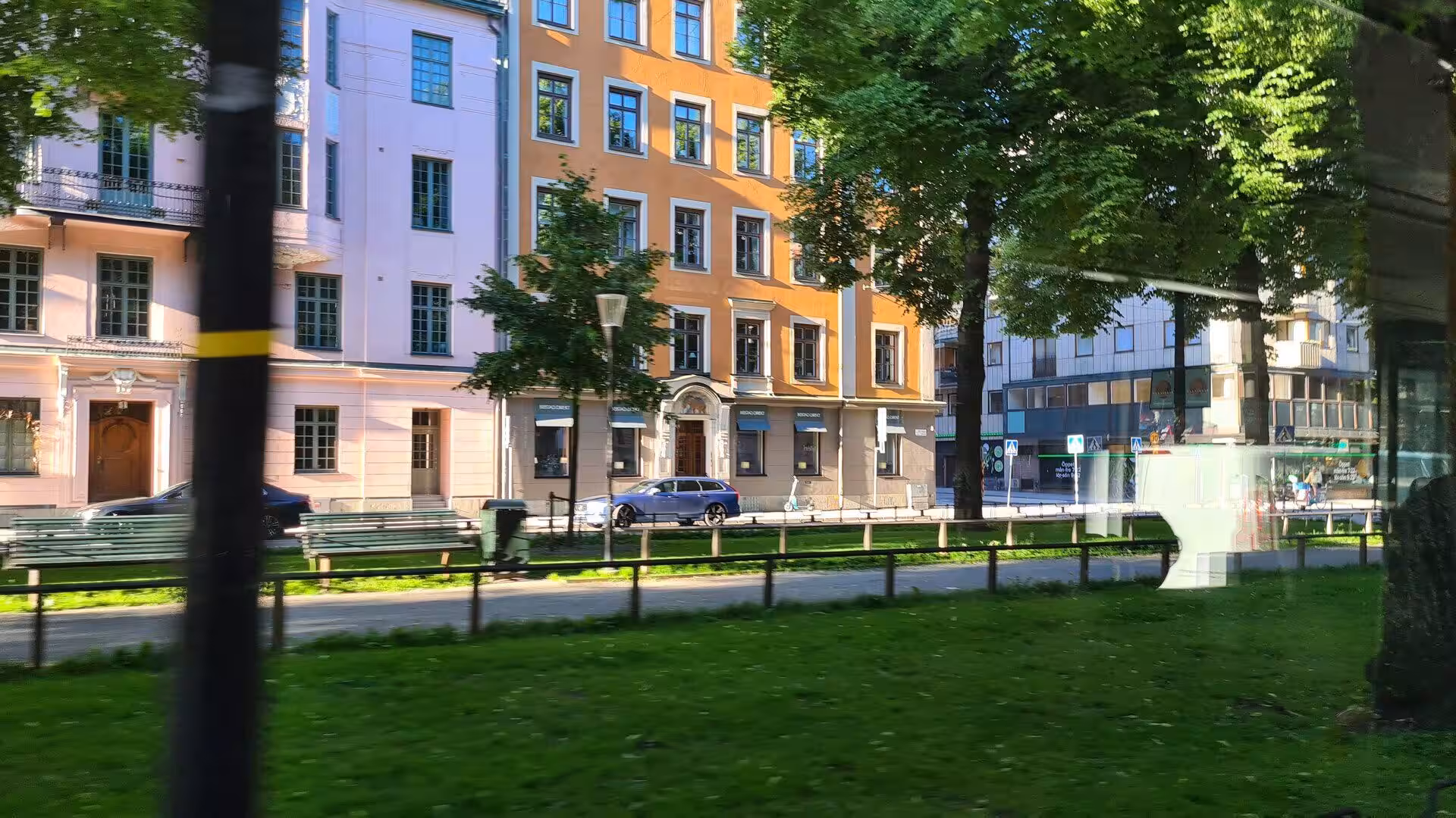 Pink and orange townhouse facades frame a quiet street with a parked car.