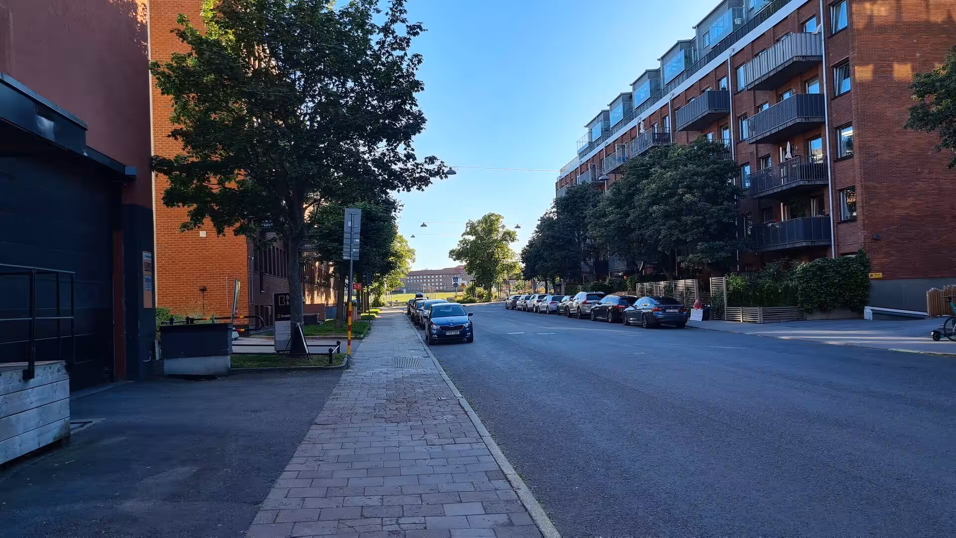 Red brick apartment blocks with balconies line a calm street of parked cars.