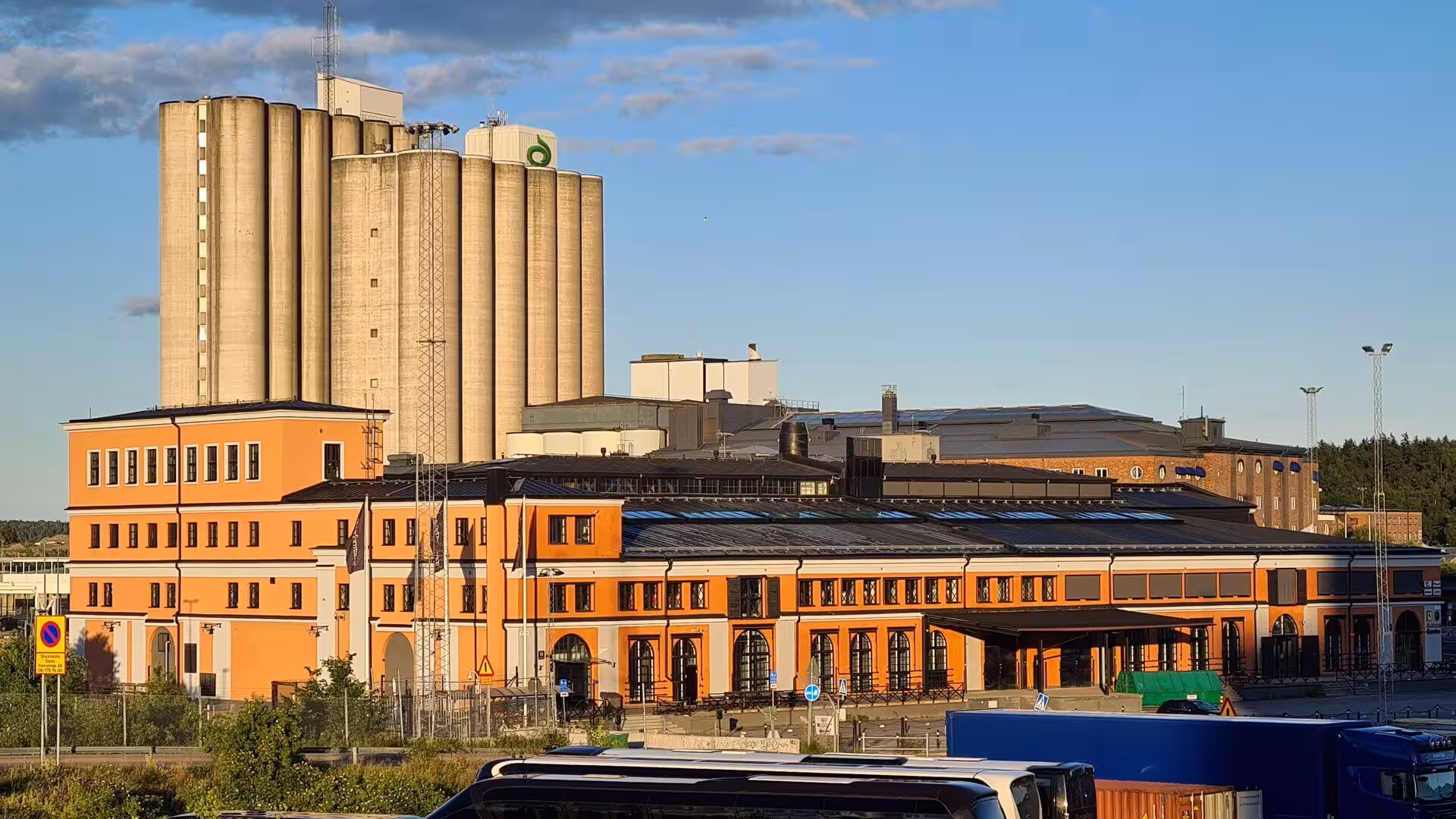 A long orange warehouse sits beneath rows of tall concrete grain silos.
