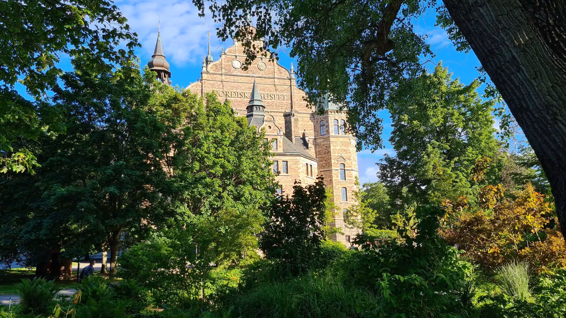 The stone facade and twin spires of the Nordic Museum rise behind leafy trees.