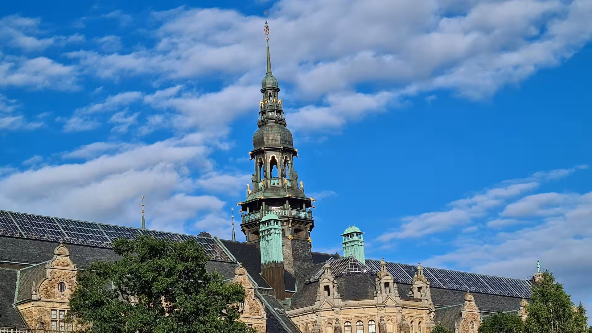 A gilded copper spire rises above an ornate historic building.