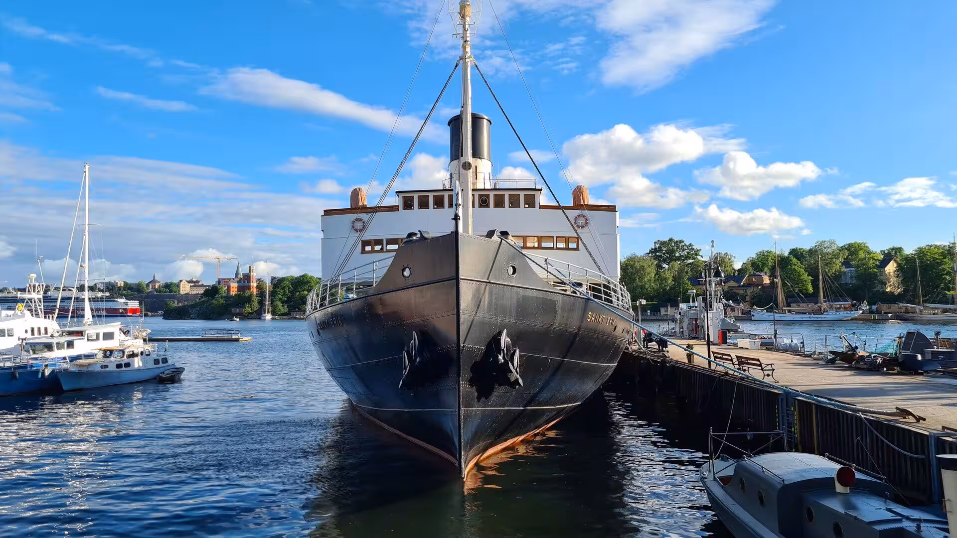 A dark steamship stands tall at the pier with its white deckhouse.