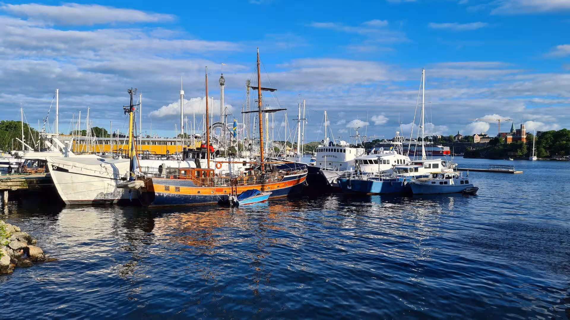 An orange-hulled wooden ship rests among the white boats of the marina.