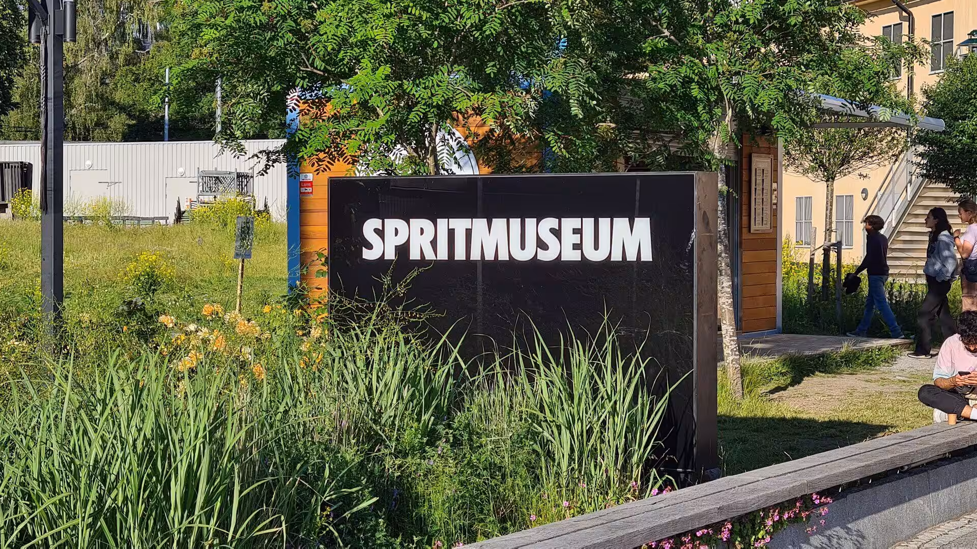The black Spritmuseum sign rises from tall grass and summer wildflowers.