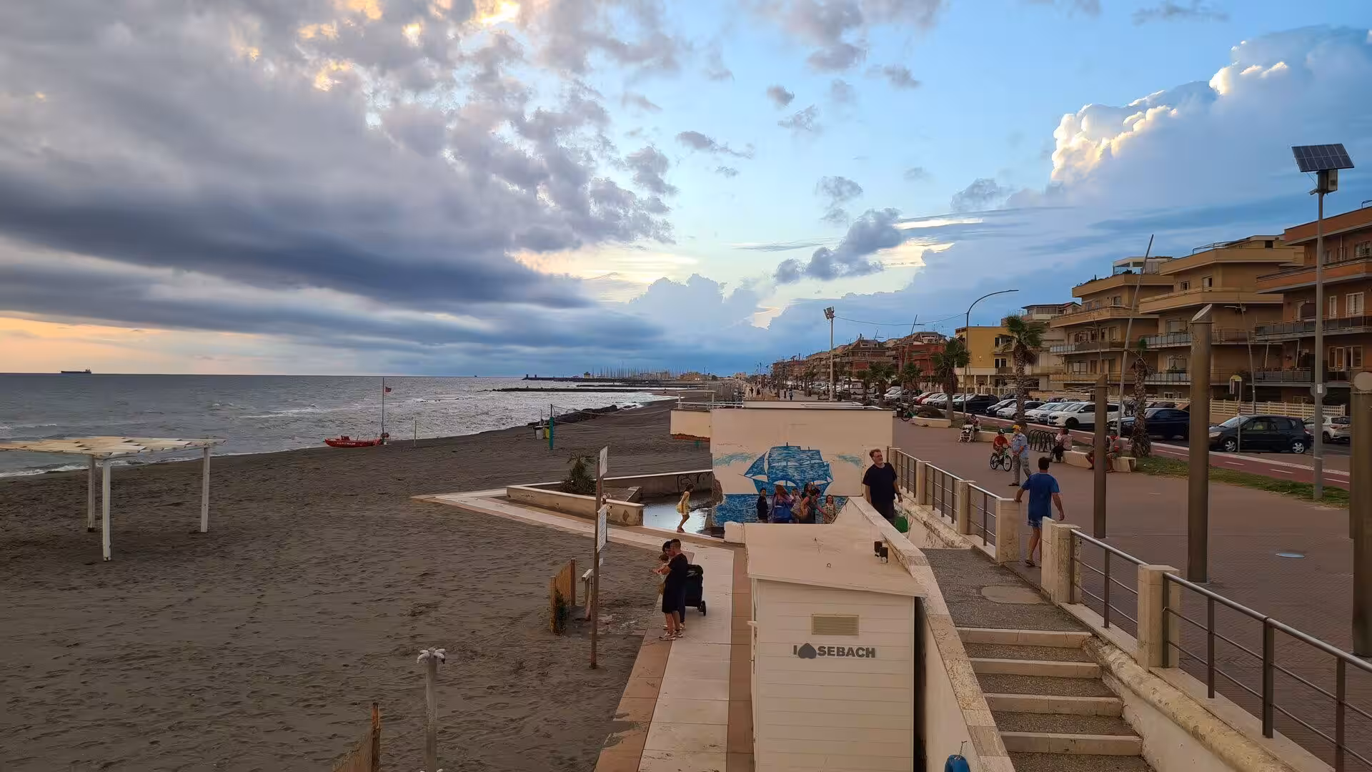 People stroll along a seaside promenade as dusk settles over the beach.