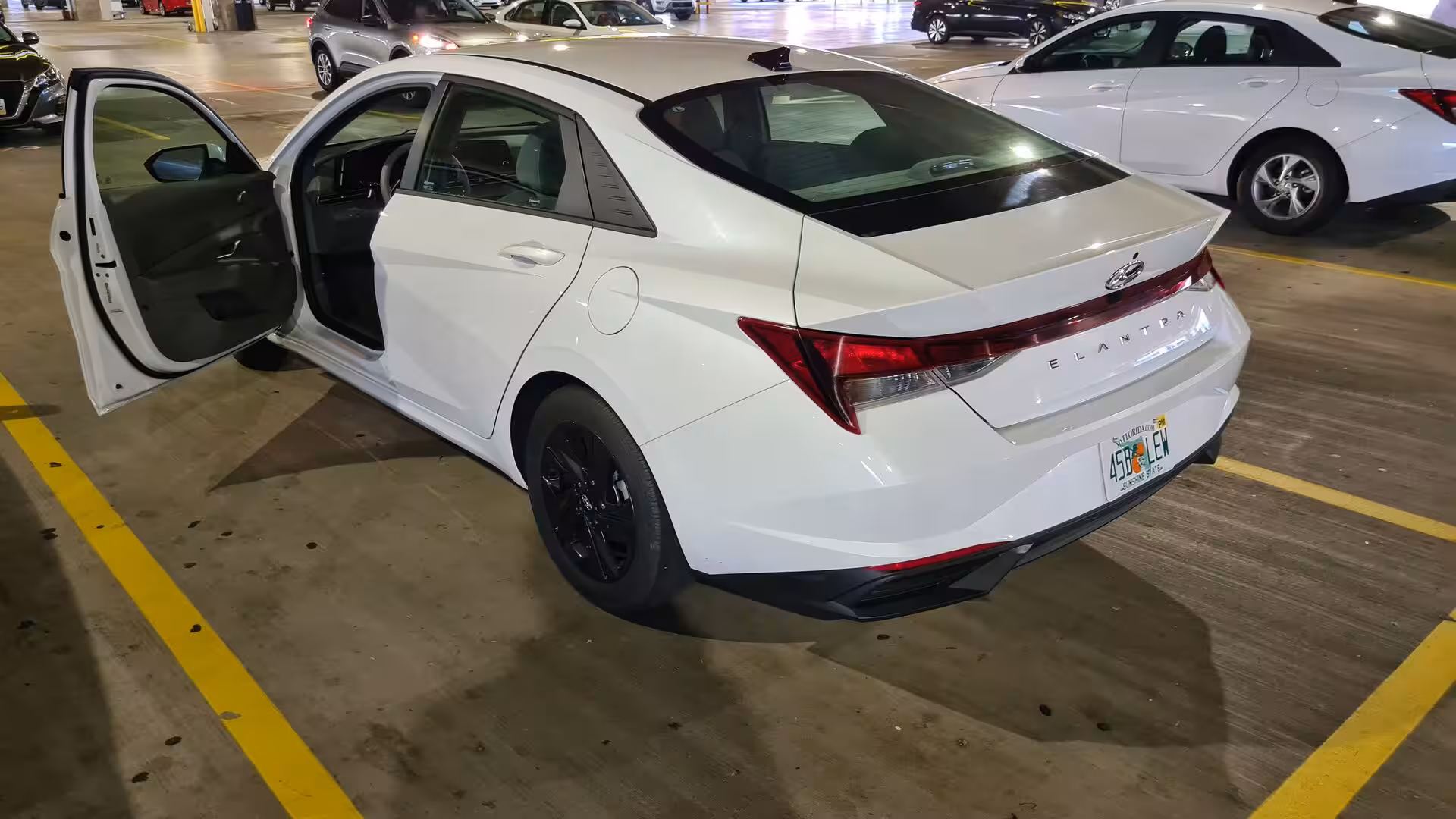 A white sedan with both doors open in a parking structure.