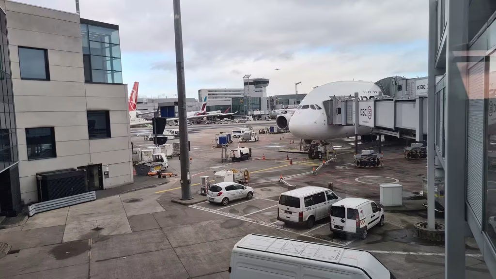 A large white double-decker passenger jet waits at the gate on a busy airport apron.