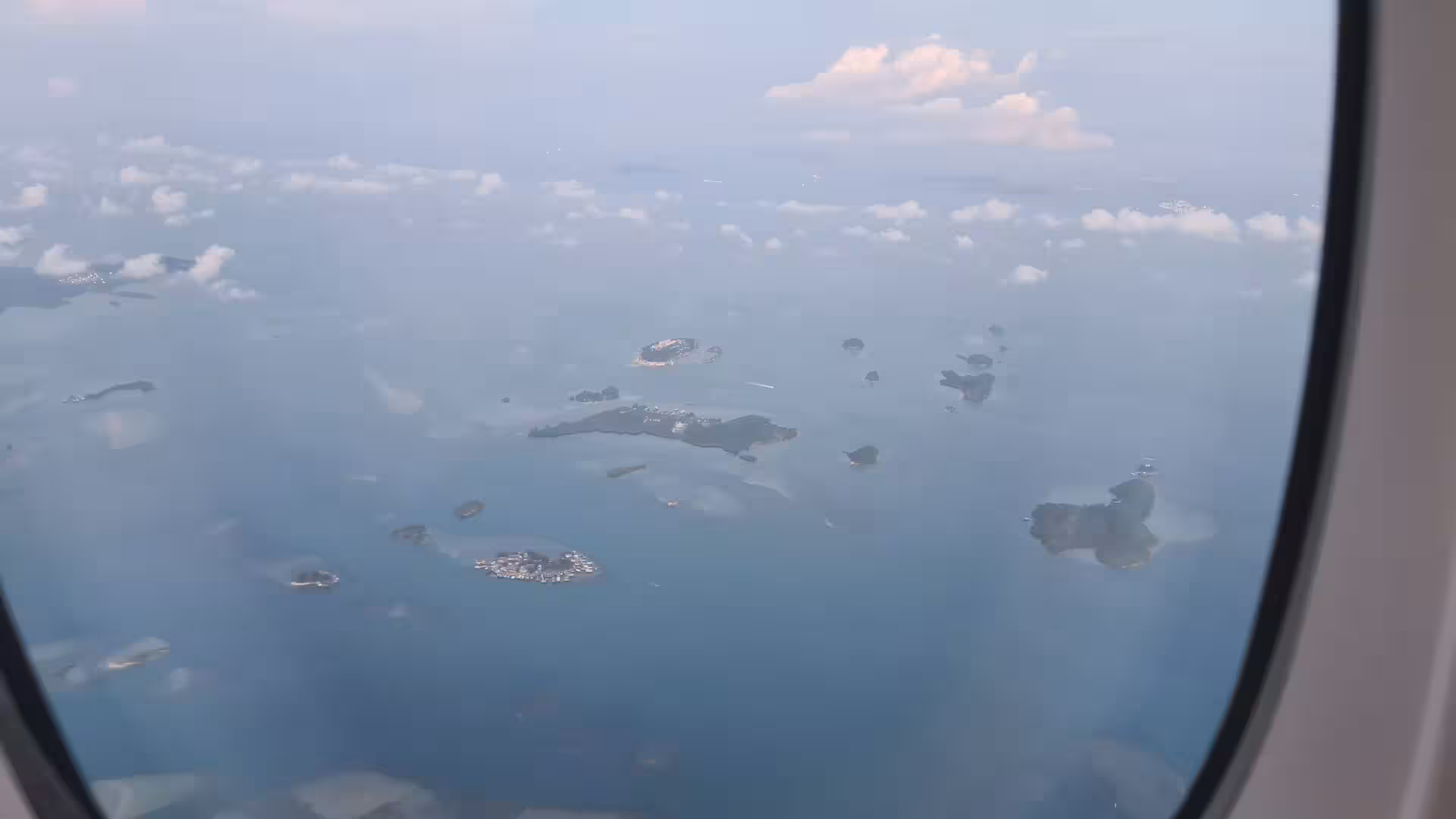 Many small isles and pale sandbanks scatter across the hazy ocean beneath the aircraft.