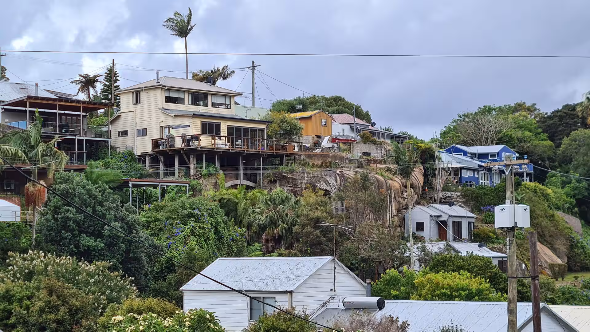 Two-storey homes with decks climb a steep, rocky hillside thick with palms and shrubs.