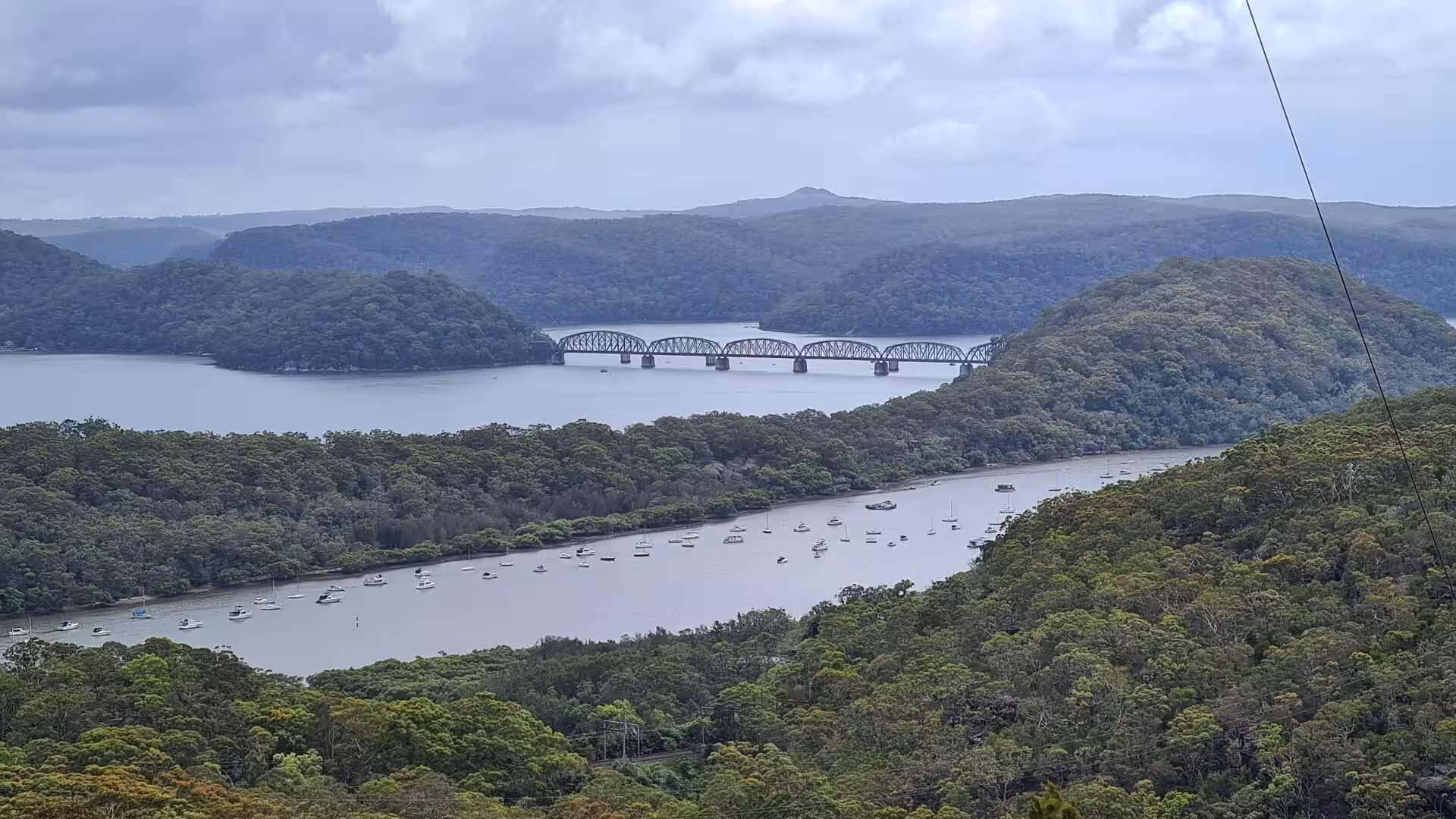 From a hillside, an estuary crowded with moored boats is crossed by a long truss bridge.