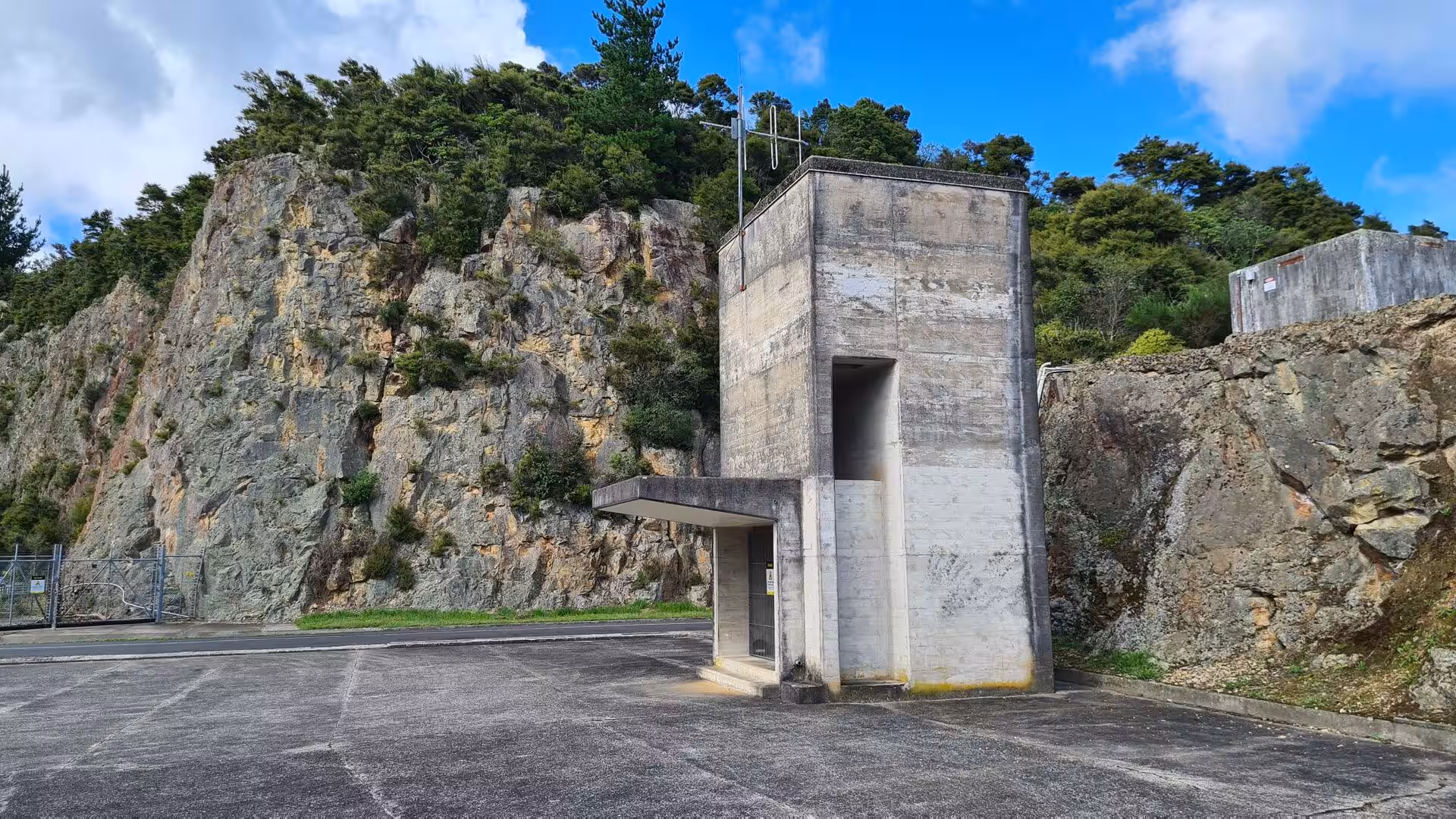 A bare concrete watchtower stands before a steep rock face.
