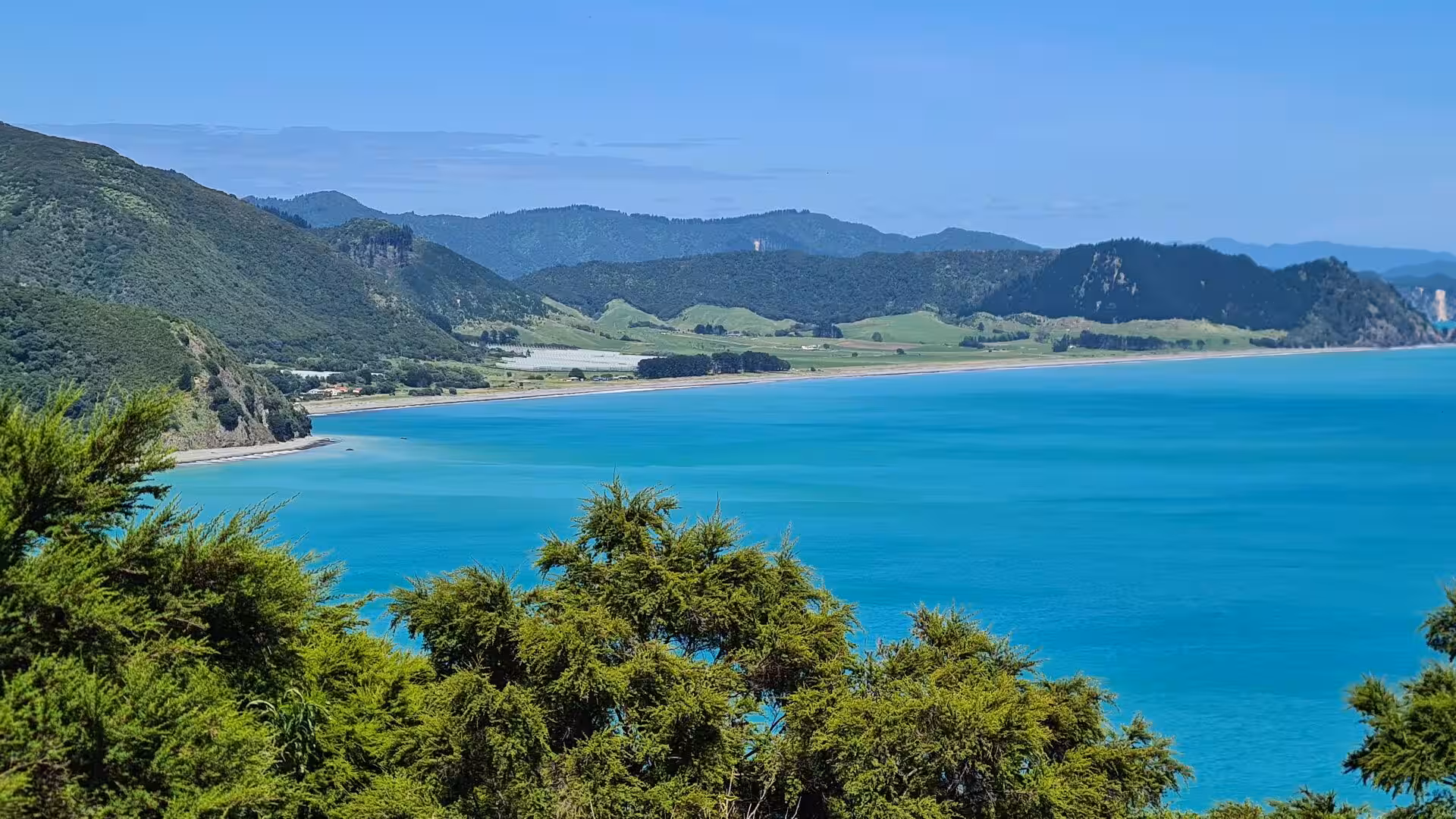A vivid turquoise bay curves beside sandy shoreline and forested hills.