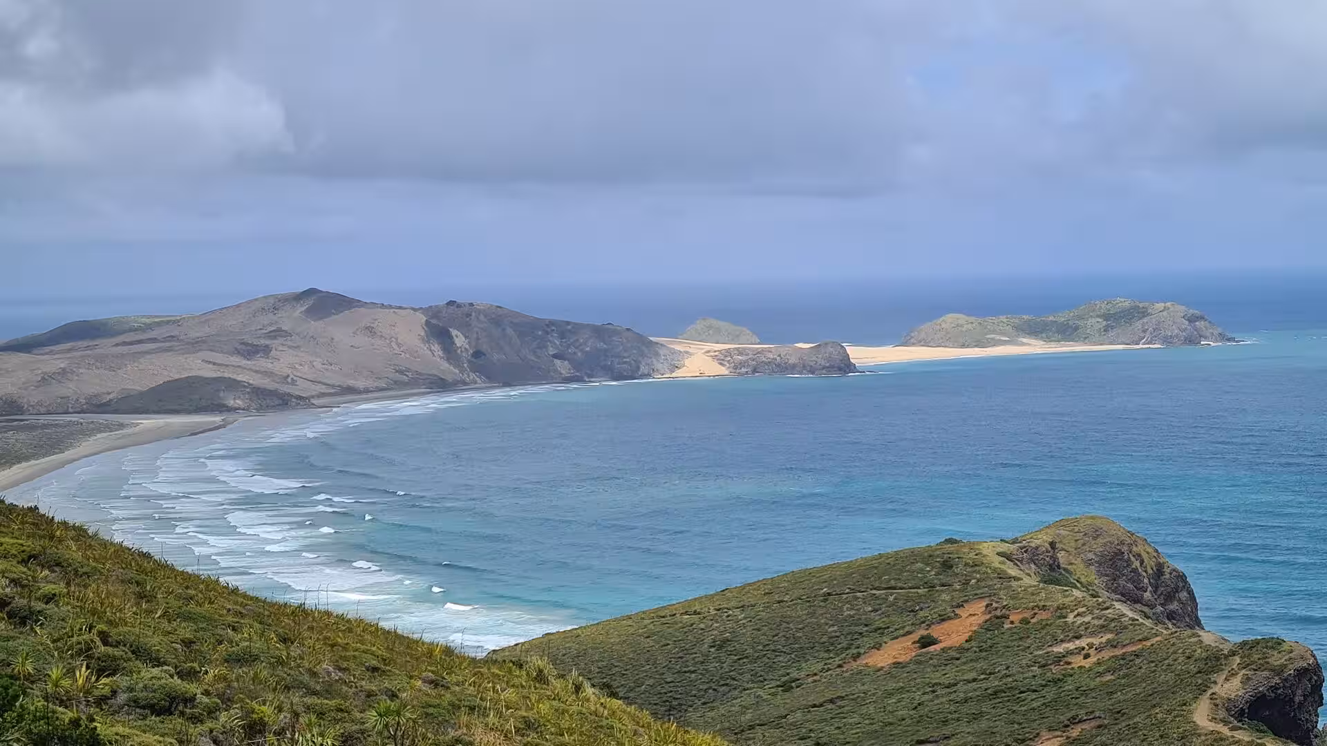 A sweeping bay with a pale sand beach and two islets seen from upslope.