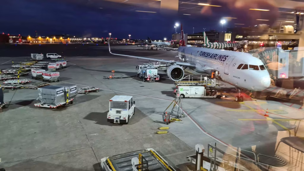 A Turkish Airlines airliner stands at the gate glistening beneath apron lights at dusk.