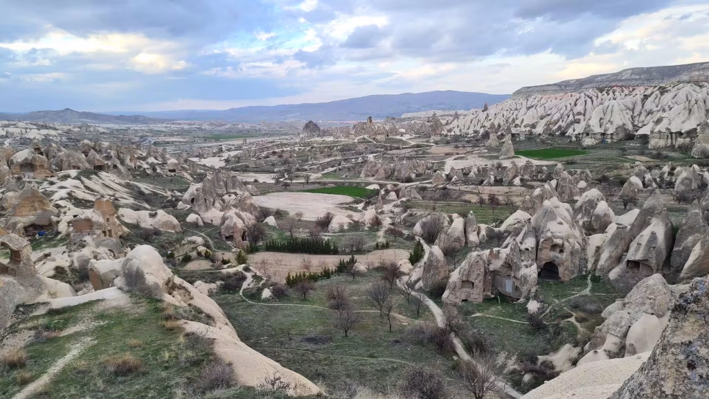 A sweeping landscape of countless cone-shaped rock towers and carved cave homes below a hazy sky.