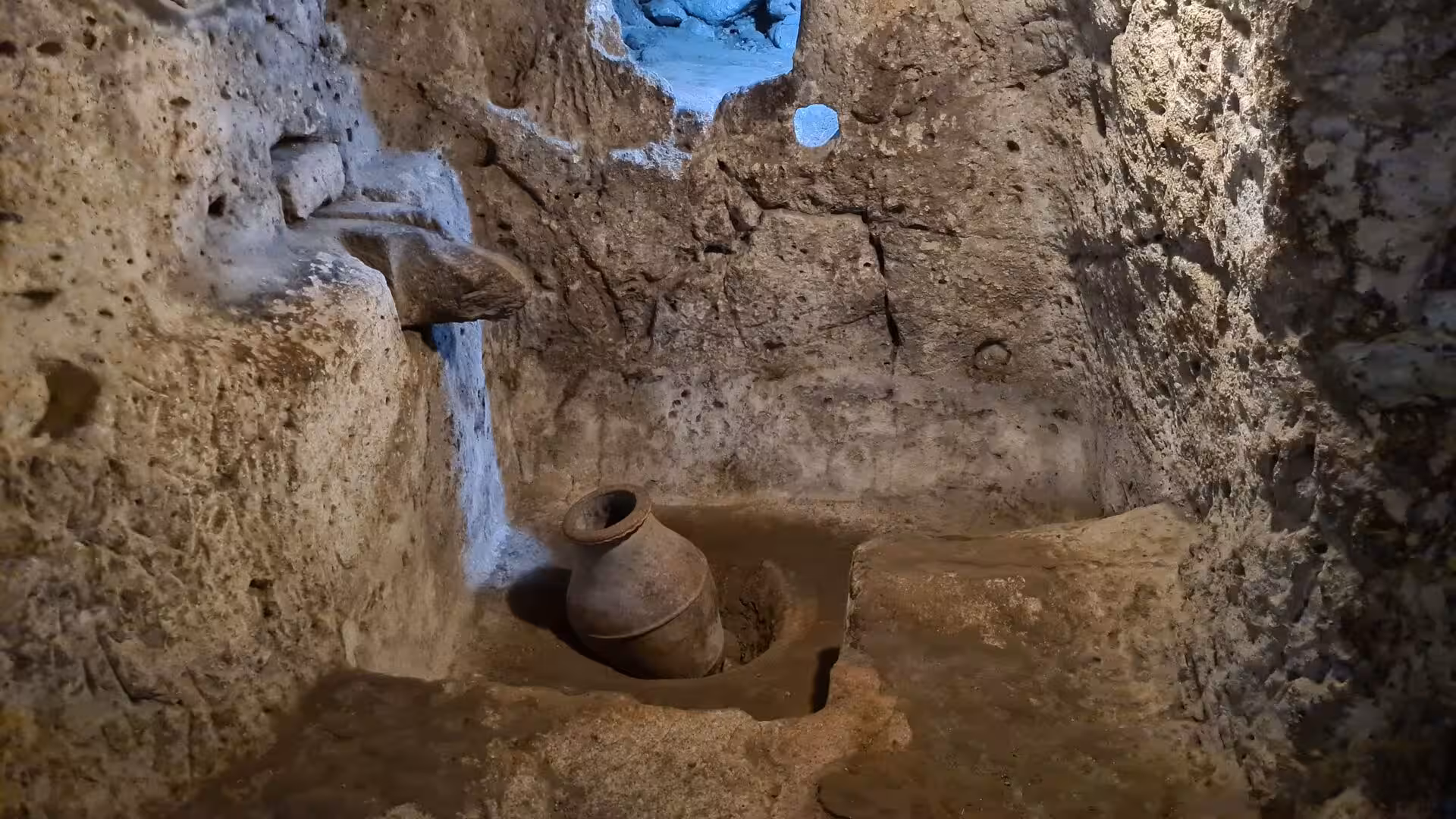 A weathered terracotta storage jar rests in a carved niche within an underground chamber.