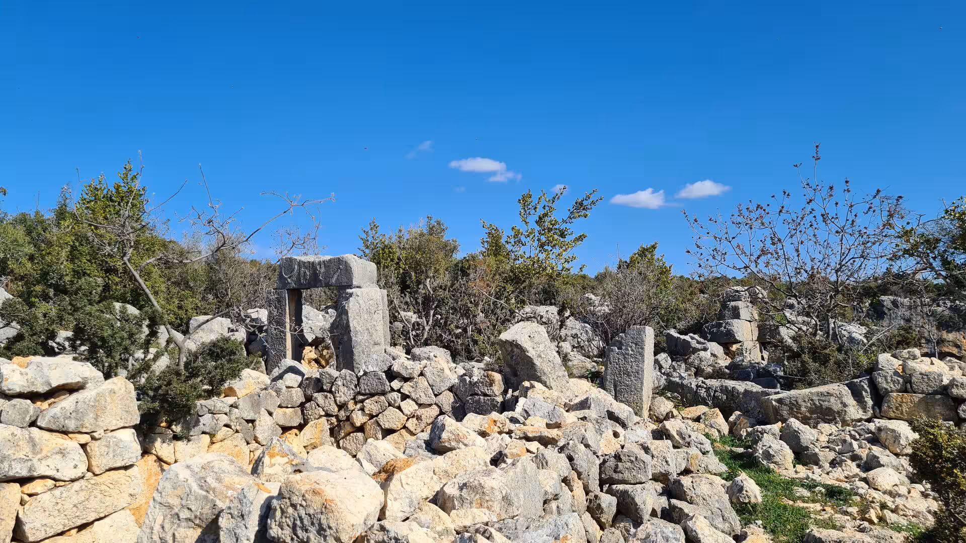 A stone trilithon stands amid scattered boulders and low scrub.