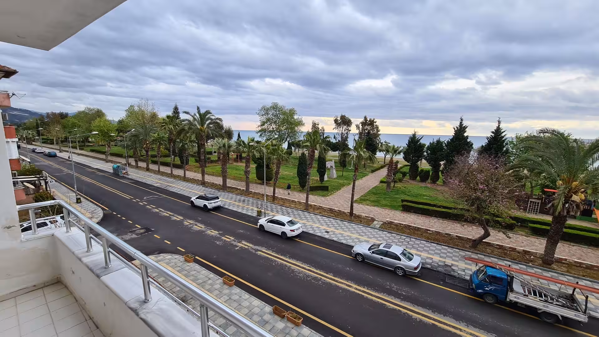 Cars drive a coastal road bordered by palm trees and green parks.